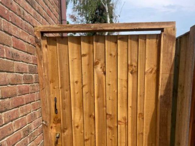 A tall closeboard side gate hung between a brick wall and a new fence