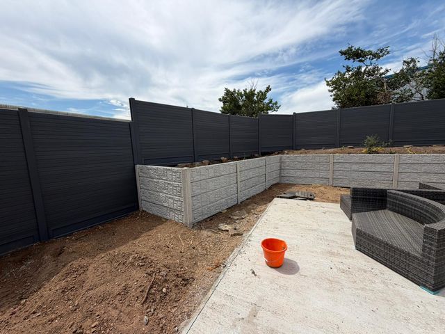 Grey composite fence panels above a textured concrete panel retaining wall around a new patio
