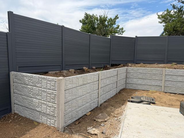 Grey composite fence panels above a textured concrete panel wall around a raised bed