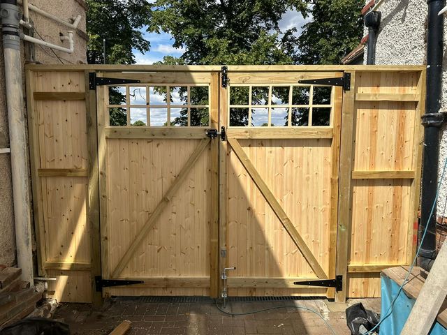 The braced inside face of a pair of timber gates with window-style tops and black strap hinges
