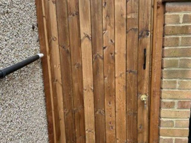 A closeboard side gate hung between a pebbledashed wall and a brick wall